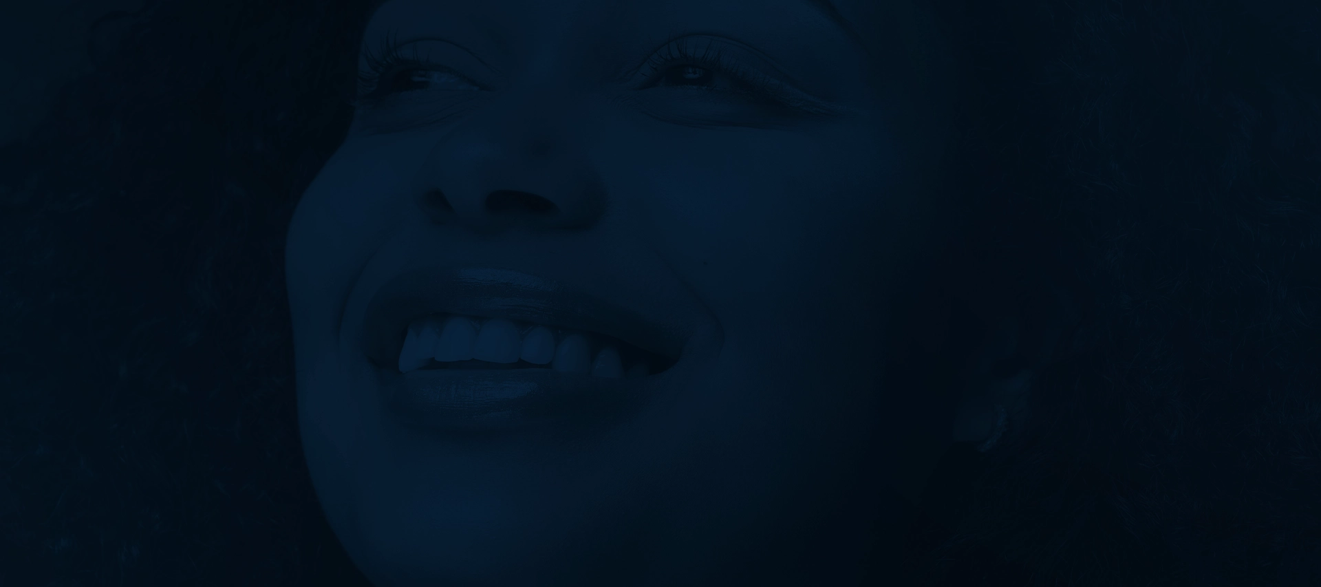 Close do sorriso de uma paciente de facetas, em tom azul-marinho sobre fundo escuro