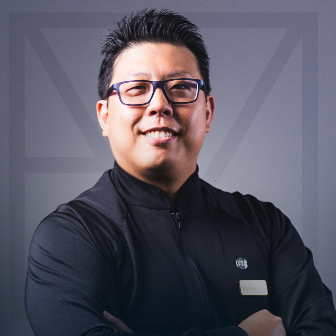Dr. Willian Akinori Saito, CEO e fundador da Clínica IEM, sorrindo de braços cruzados com o uniforme preto da equipe