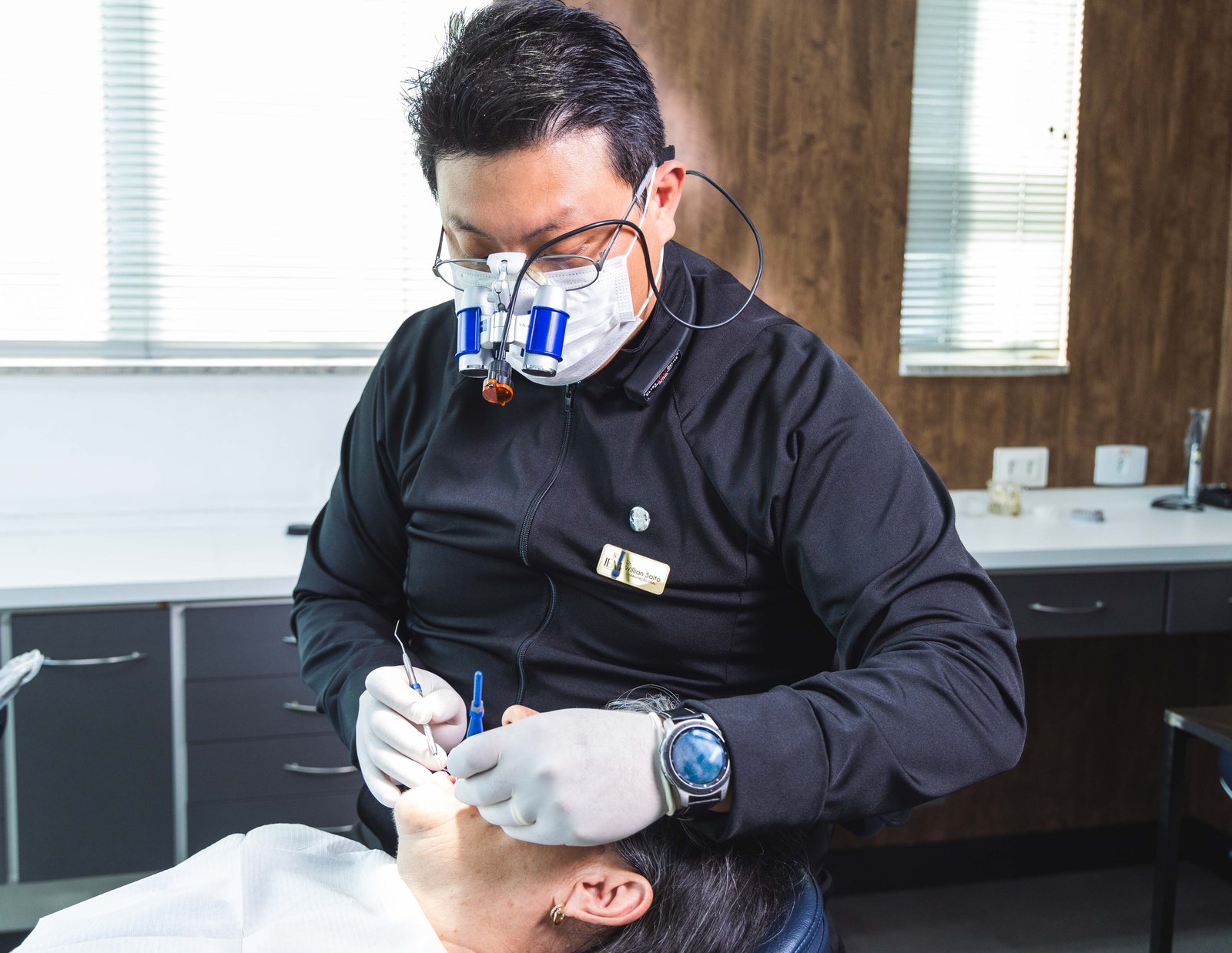 Dr. Willian Saito executando procedimento clínico com lupas de magnificação e máscara