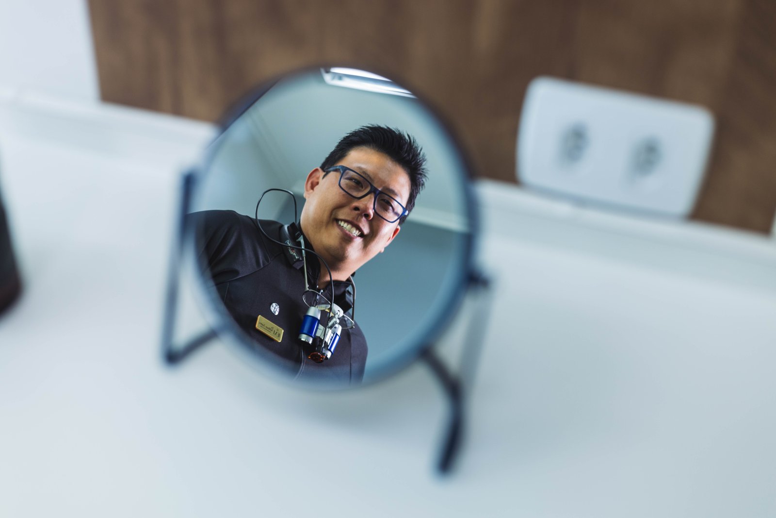 Reflexo do Dr. Willian Saito sorrindo em espelho de consultório da clínica